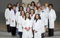 Twenty nursing faculty members smiling and wearing nurse practitioner coats.